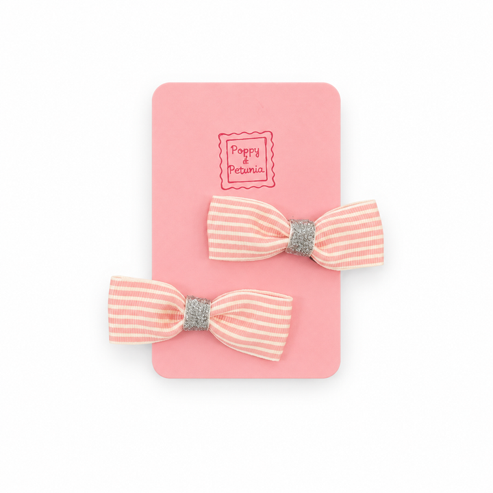 Two pink and cream striped mini bow hair clips with silver glitter centers on a pink Poppy + Petunia display card.